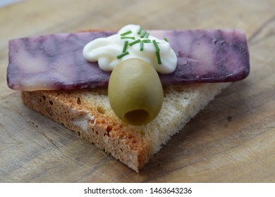 Thin Cut Of Port Wine Derby Cheese On A Crispy Slice Of Bread With Two Green Olives And A Dollop Of Sauce 