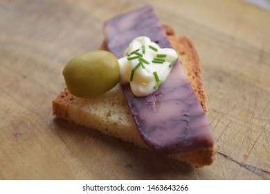 Thin Cut Of Port Wine Derby Cheese On A Crispy Slice Of Bread With Two Green Olives And A Dollop Of Sauce 