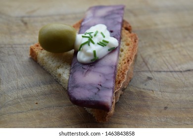 Thin Cut Of Port Wine Derby Cheese On A Crispy Slice Of Bread With Two Green Olives And A Dollop Of Sauce 