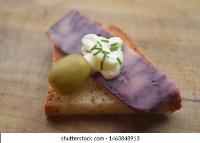 Thin Cut Of Port Wine Derby Cheese On A Crispy Slice Of Bread With Two Green Olives And A Dollop Of Sauce 