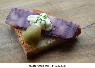 Thin Cut Of Port Wine Derby Cheese On A Crispy Slice Of Bread With Two Green Olives And A Dollop Of Sauce 