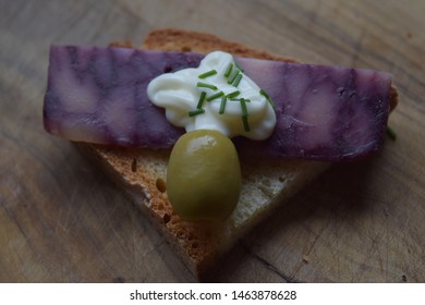 Thin Cut Of Port Wine Derby Cheese On A Crispy Slice Of Bread With Two Green Olives And A Dollop Of Sauce 