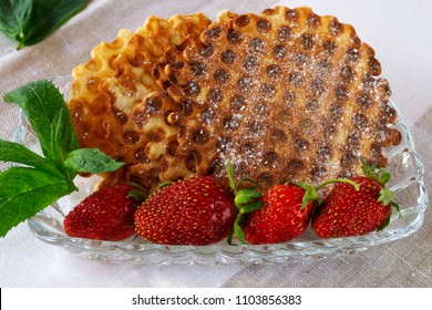 Thin Home-made Wafers Sprinkled With Powdered Sugar, Laid On A Glass Plate With Leaves Of Green Mint And Ripe Red Strawberries.