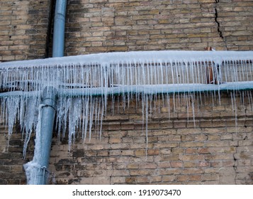 Thin icicles on the old crack brick wall.Drain pipe.