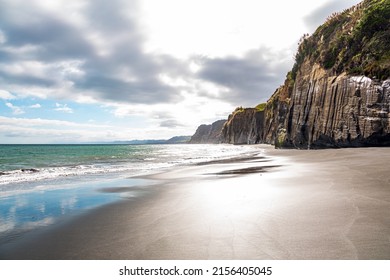 Thin layer of water on smooth sand reflects the sky. Low tide in the Pacific Ocean. The magnificent nature of New Zealand. Sheer White Cliffs of the Pacific coast of northern Taranaki