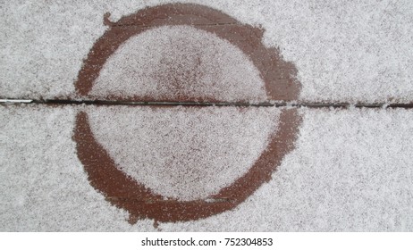 Thin layer of white freshly fallen snow covering stained brown wooden deck leaving a circle mark after the first snow fall of the winter