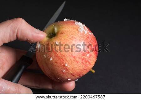 Thin layer white wax scraped with knife from the surface of a store-bought fresh apple. How to extend product shelf life? Waxing an apple. Black background. Food industry theme.