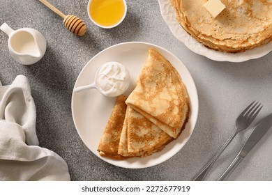 Thin pancakes or russian blini with butter , honey, sour cream on gray stone background. Top view.