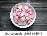 Thin radish slices in a white plate on rustic wooden table. Vegetable salad. Food photography