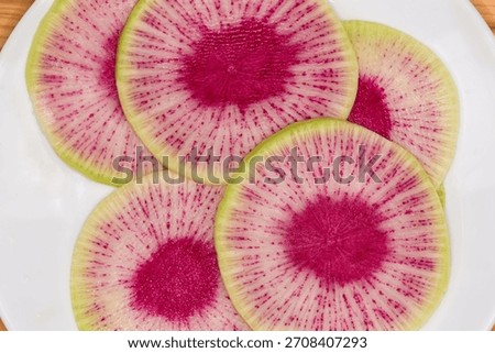 Thin round slices of radish Red Mit variety, also known as watermelon radish with white-green skin, pink flesh and mild flavor without bitterness, top view close-up 