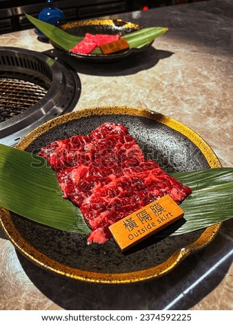Thin sliced raw beef A5 wagyu outside skirt presented on top of green leaf and black and gold plate on top of ceramic table