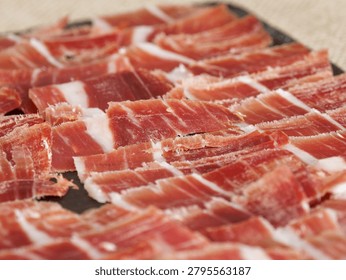 Thin slices of cured ham elegantly arranged on a serving tray, ideal for gourmet dining, catering events, Spanish cuisine and charcuterie concepts.