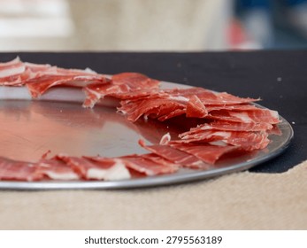 Thin slices of cured ham elegantly arranged on a serving tray, ideal for gourmet dining, catering events, Spanish cuisine and charcuterie concepts.