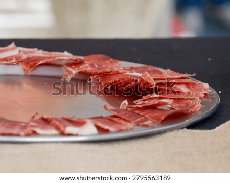 Thin slices of cured ham elegantly arranged on a serving tray, ideal for gourmet dining, catering events, Spanish cuisine and charcuterie concepts.