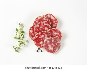 Thin Slices Of French Dry Salami, Thyme And Peppercorns On White Background