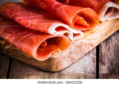 thin slices of prosciutto closeup on wooden cutting board - Powered by Shutterstock