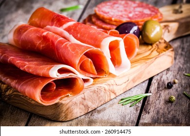 thin slices of prosciutto with olives and salami on wooden cutting board - Powered by Shutterstock