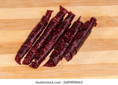Thin soft flexible raspberry pastila made with dried raspberry pulp twisted into tubes on a wooden bamboo cutting board, top view close-up