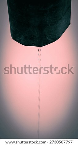 A thin stream of water gracefully flows from a dark metal pipe, creating delicate ripples as it connects with the serene pink backdrop, embodying tranquility and simplicity.