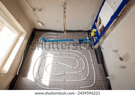 Thin white tubes are bended in complex curve of new brass, distribution system manifold mounted for central heating floor in unfinished bathroom, residential building under construction.