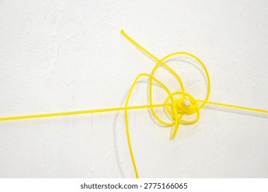 a thin yellow nylon string tangled on a white textured wall. Close up of a bright synthetic cord coiled and knotted against a plain background for industrial or household concept.