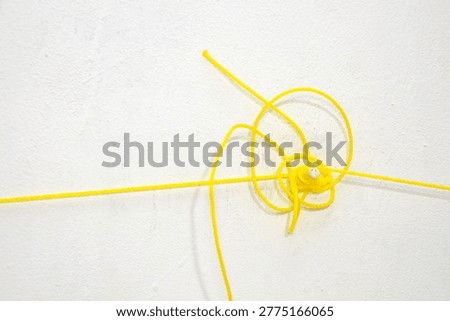 a thin yellow nylon string tangled on a white textured wall. Close up of a bright synthetic cord coiled and knotted against a plain background for industrial or household concept.