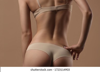 Thin young woman in underwear on beige background. Back view. Fitness, diet, skin and body care