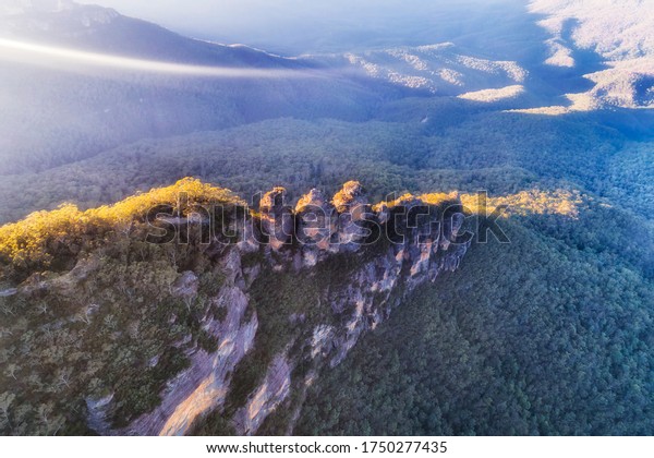 Thing line\
of sun light on top of Three Sisters rock formation in BLue\
Moutains of Australia - elevated aerial\
view.