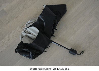 Things are objects of constant use. A beautiful beige, gray umbrella with a black lining and a cover lies folded on a beige wooden floor, natural parquet.