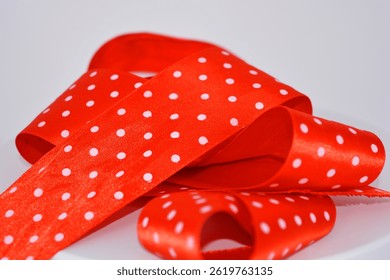 Things, objects, materials are interestingly laid out and twisted on a white surface. Bright red satin ribbons with white polka dots are located on a white plastic background.