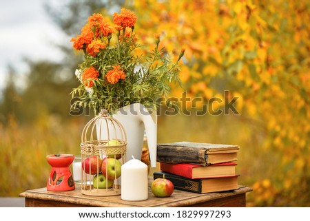 Things in retro style stand: old books, candles, apples, flowers marigolds. Autumn background