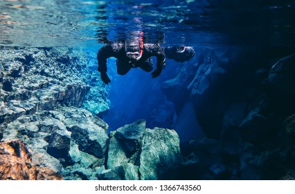 Thingvellir, Silfra / Iceland - April 5th 2019: Snorkelers And Scuba Divers Swimming In Famous Popular Fissure Drift With Blue Crystal Clear Glacial Water Between Tectonic Plates Mid Atlantic Ridge