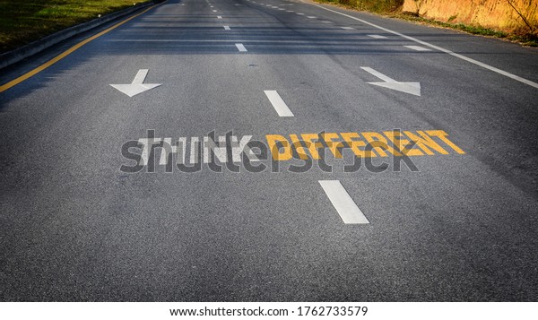 Think different word with white arrow and dividing\
lines on black asphalt road surface, business challenge concept and\
success idea
