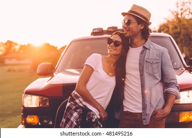 Thinking about new place to go. Beautiful young smiling couple looking thoughtful while bonding to each other and leaning at their pick-up truck 