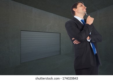 Thinking businessman holding pen against dark grey room