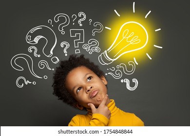 Thinking child boy on black background with light bulb and question marks. Brainstorming and idea concept