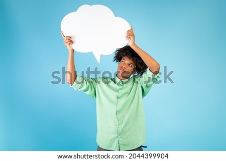 Thinking concept. Pensive african american guy holding and looking at speech bubble, pondering, posing on blue background, free space for text. Thoughtful male student with empty word cloud