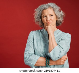 Thinking, Confused And Wondering Woman Looking Puzzled, Unsure And Uncertain About Choice, Decision And Idea In Mind Against Studio Red Background. Thoughtful Senior Woman With Goofy Frown