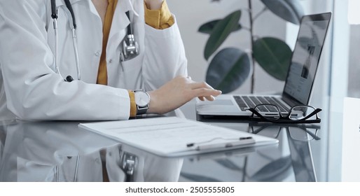 Thinking doctor woman is reviewing medical records on laptop. Close-up of a healthcare unknown professional analyzing patient information on a computer. Medicine - Powered by Shutterstock