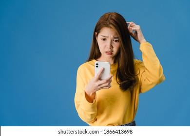 Thinking Dreaming Young Asia Lady Using Phone With Positive Expression, Dressed In Casual Clothing Feeling Happiness And Stand Isolated On Blue Background. Happy Adorable Glad Woman Rejoices Success.