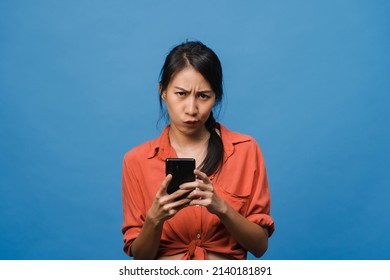 Thinking dreaming young Asia lady using phone with positive expression, dressed in casual clothing feeling happiness and stand isolated on blue background. Happy adorable glad woman rejoices success. - Shutterstock ID 2140181891
