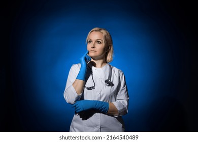 Thinking Female Doctor In A White Coat, Gloves, With A Stethoscope On A Dark Background