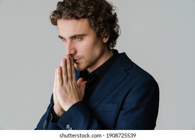 Thinking handsome man in jacket holding palms together isolated over white background
