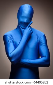 Thinking Man With Hand On Chin Wearing Full Blue Nylon Bodysuit On A Grey Background.