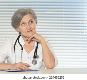 Thinking Senior Doctor Woman Sitting At Table