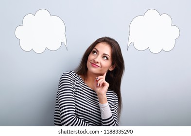 Thinking smiling young woman looking up on two empty choice bubble above on blue background with empty copy space