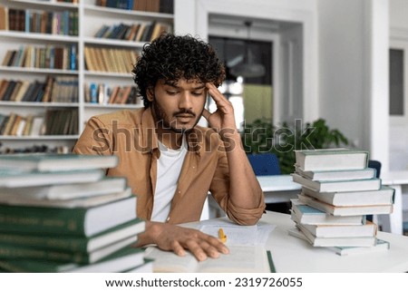 Thinking student preparing for exams inside academic library, man overworked and tired studying alone, hispanic sitting among books doing homework.