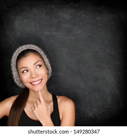 Thinking Woman By Blackboard. Multiracial Hipster University College Student Pensive And Contemplating Looking Up To The At Empty Blank Copy Space On Chalkboard Black Background. Asian Caucasian, 20s.