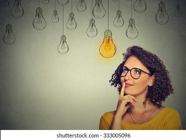Thinking woman in glasses looking up with light idea bulb above head isolated on gray wall background