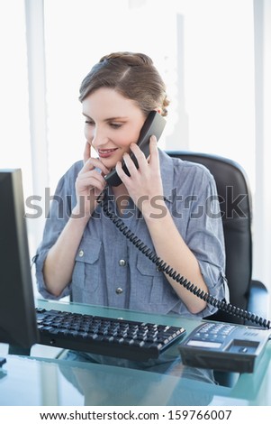 Thinking young businesswoman phoning while sitting a desk in office